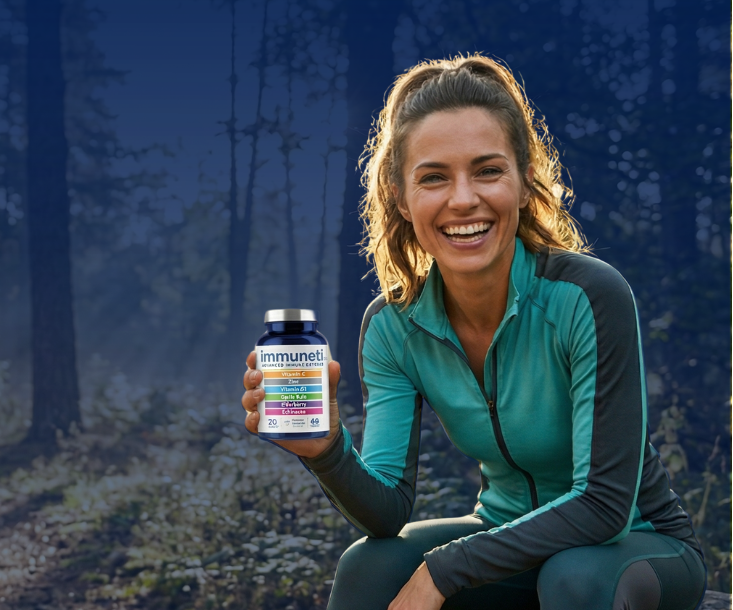 Active woman smiling in a forest holding Immuneti supplement, representing daily immune support and overall wellness
